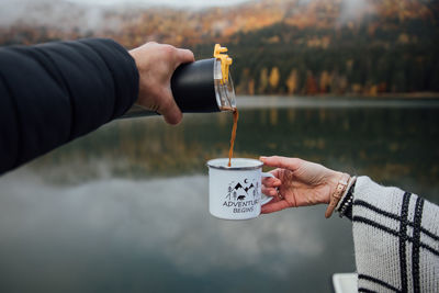 Midsection of man holding coffee cup by lake