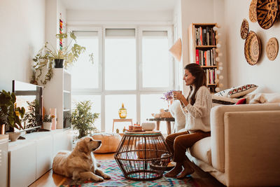 Side view of woman looking at dog while sitting on sofa