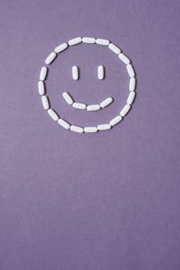 Directly above shot of medicines in smiley face shape on purple background