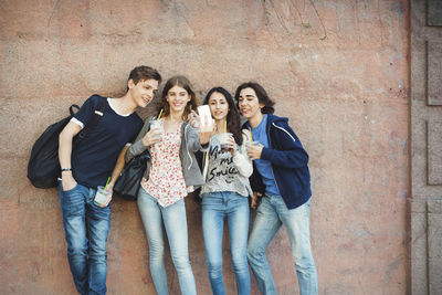 Happy teenagers taking selfie against wall