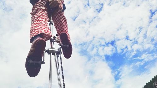 Low section of man riding unicycle against cloudy sky