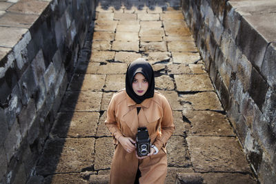 Muslim tourist woman wearing hijab / headscarf and brown coat at ratu boko temple, yogyakarta