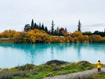 Rear view of woman standing by lake against sky during autumn