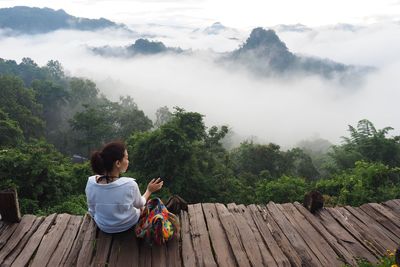 Young woman sitting on wood against sky