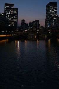Illuminated buildings by river against sky in city at night