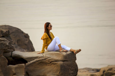 Woman sitting on rock at beach against clear sky
