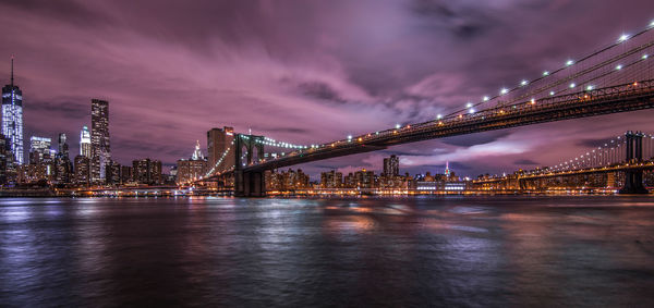 Illuminated bridge over river with city in background