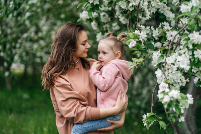 Young mother with her daughter in her arms in a blooming apple orchard