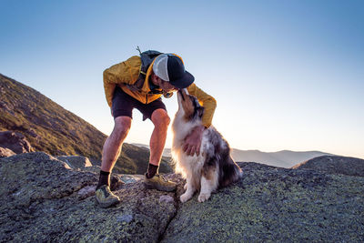 Man with dog on rock against sky