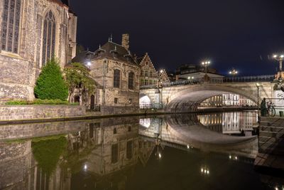 Illuminated bridge over river by buildings against sky at night