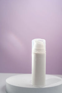 Cosmetic bottle with water splashes on a purple background.