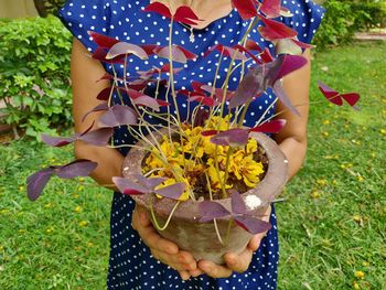 Midsection of woman holding flower on field