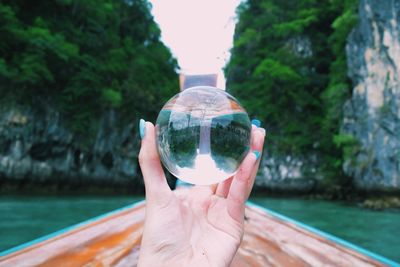 Cropped image of hand holding crystal ball in swimming pool