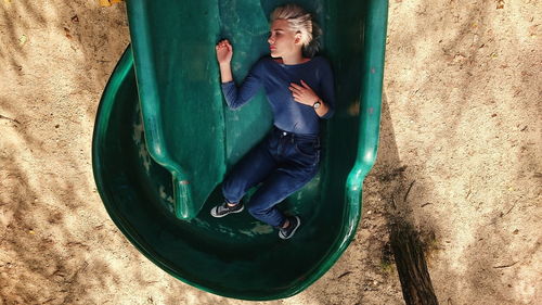 Directly above shot of sad young woman lying in green slide at playground