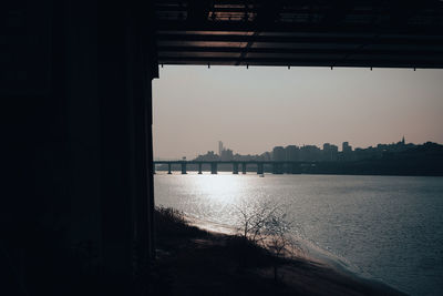 Silhouette buildings by river against sky during sunset