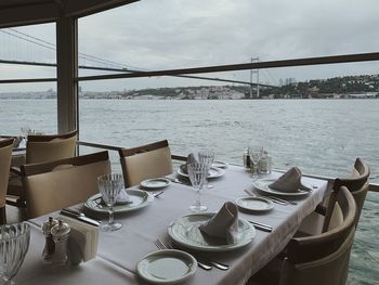 Chairs and table at restaurant by sea against sky