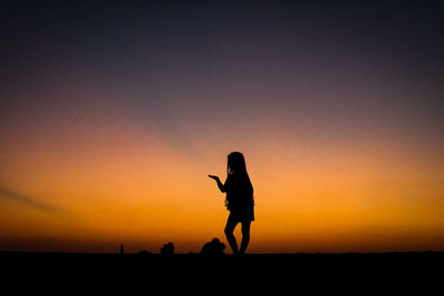 Silhouette of woman standing against sky during sunset