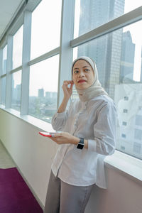 Portrait of woman standing against window