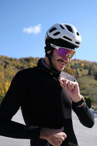 Cyclist with a white helmet in nature smiling while zipping up his cycling jersey