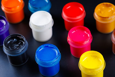 Full-frame close-up view d of opened small gouache paint jars on black surface