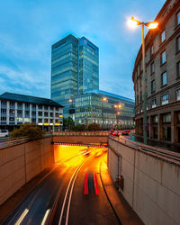 Light trails on road amidst buildings in city at dusk