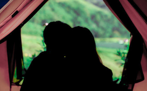 Rear view of couple kissing against window