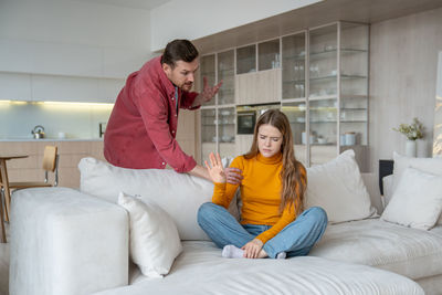 Side view of young woman using phone while sitting on bed at home