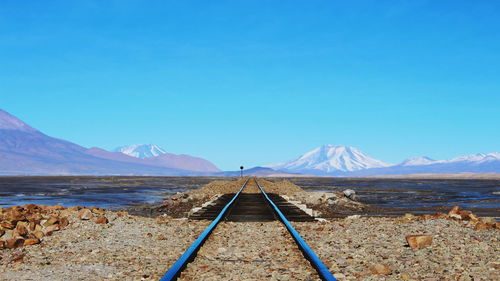 Railroad tracks leading towards mountains against clear blue sky