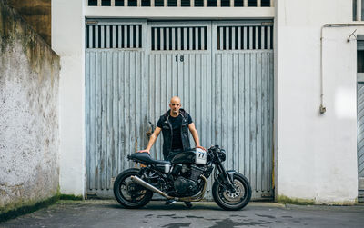 Portrait of mature man with motorcycle standing against closed garage