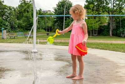 Little child playing with water at splash pad in the local public park playground in summer.