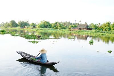 Woman sitting on rowboat in river against sky