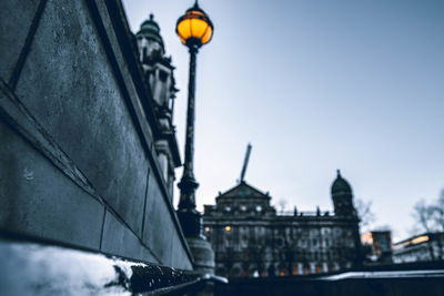 Low angle view of illuminated street light by building against sky