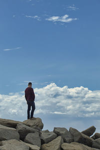 Standing man on top of a stone breakwater looking at the horizon with clouds in the background