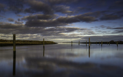 Wooden posts in lake against sky at sunset