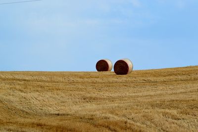 Hay bales on field against clear blue sky