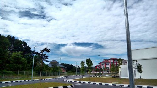 Road passing through city against cloudy sky