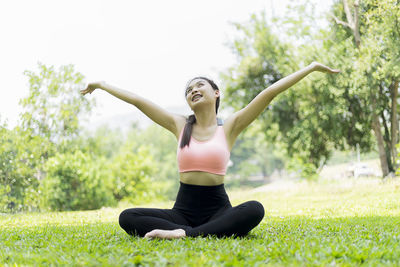 Full length of woman practicing yoga while sitting on grassy field at park