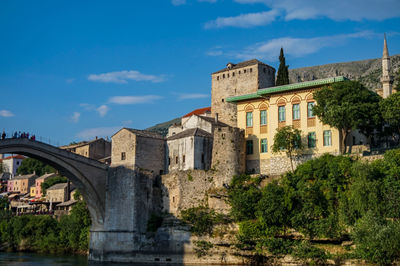 Arch bridge over river amidst buildings in city against sky