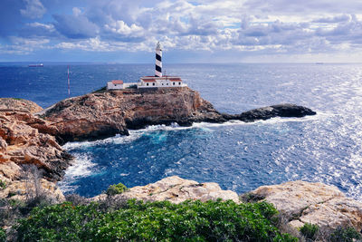 Lighthouse on rock by sea against sky