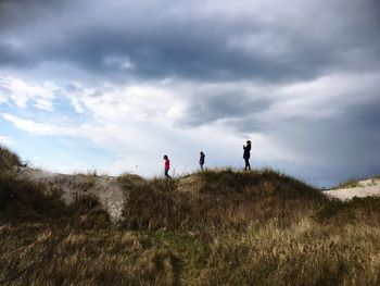 Side view of mother and daughters standing at beach against cloudy sky