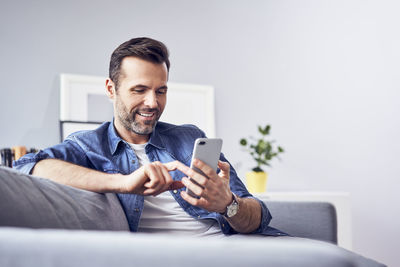 Smiling man sitting on sofa using cell phone