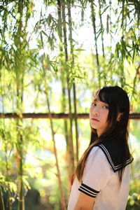 Portrait of young woman standing against trees