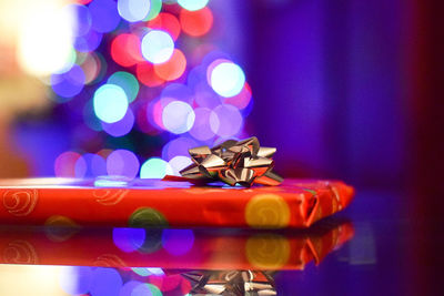 Close-up of wrapped christmas present on table against lights