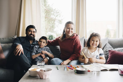 Portrait of smiling family sitting on sofa against window at home