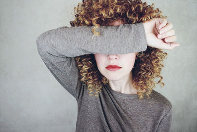 Young woman covering eyes with hand against gray background