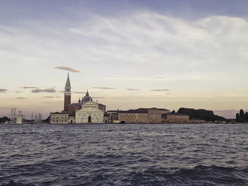 Buildings at waterfront against cloudy sky