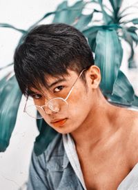 Close-up portrait of young man wearing eyeglasses against plants