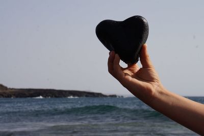 Close-up of hand holding sea against sky at beach