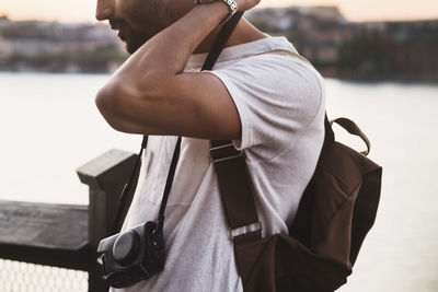 Male tourist wearing camera strap around neck while standing by river