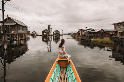 Rear view of woman on boat in canal amidst buildings against sky